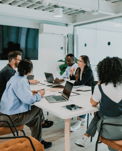 ✅ Texte alternatif (Alt text) Réunion professionnelle dans une salle moderne avec plusieurs personnes assises autour d’une table, utilisant des ordinateurs portables et discutant en groupe.