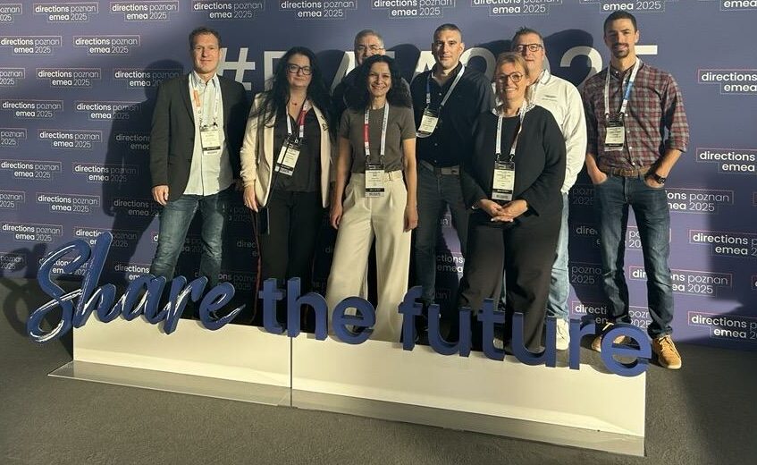 Groupe de participants devant le mur officiel Directions EMEA 2025 à Poznań, avec le slogan “Share the future” en premier plan